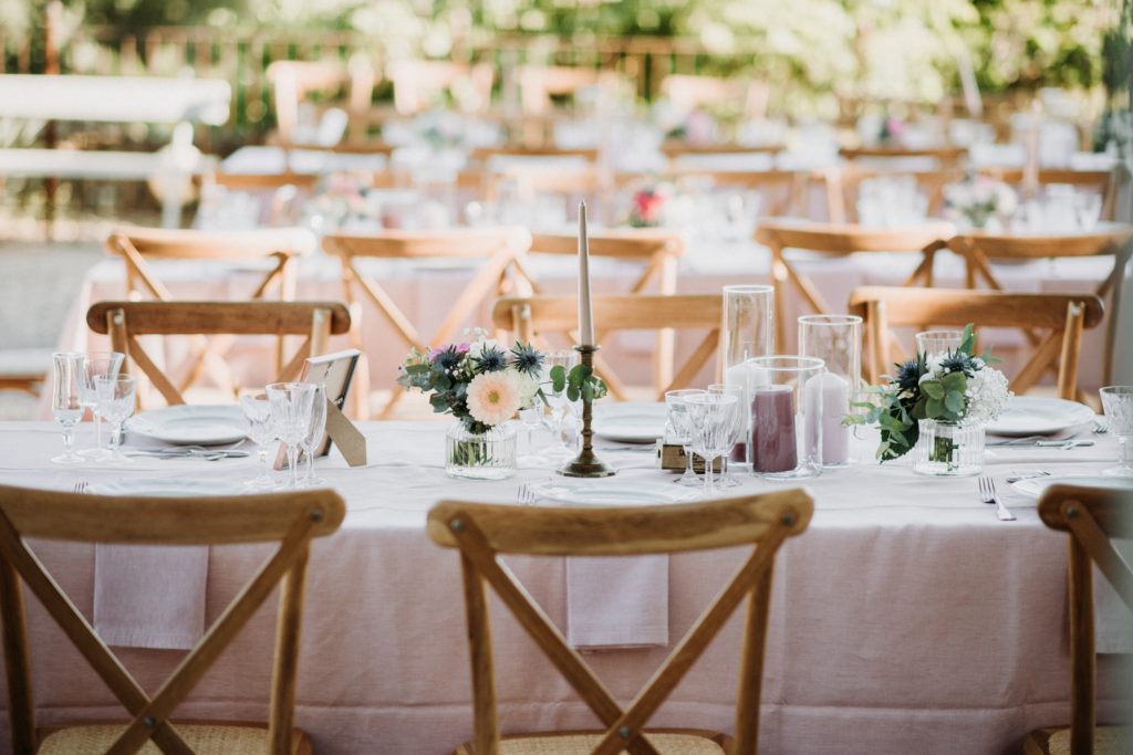 Tables d’une réception de mariage en plein air, chaises en bois et bouquets champêtres